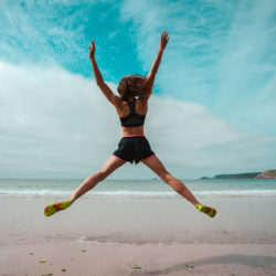 Young woman doing star jumps on the beach