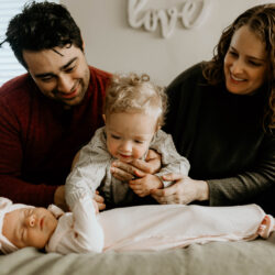 Sitting on their bed, Jeffrey and Amanda hold Micah who is patting his little sister Lilah dressed in pink | LLU Center for Fertility & IVF | Loma Linda, CA