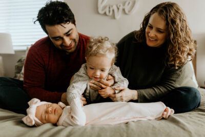 Sitting on their bed, Jeffrey and Amanda hold Micah who is patting his little sister Lilah dressed in pink | LLU Center for Fertility & IVF | Loma Linda, CA