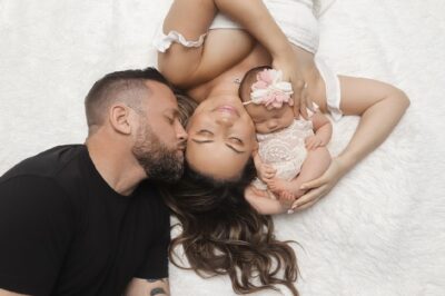 Amy lying on a bed with her husband and baby Ava, who was born with assisted reproductive technology | LLU Center for Fertility & IVF | Loma Linda, CA